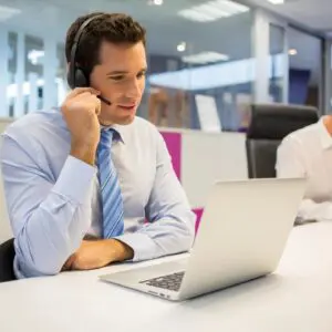 A person sitting in front of a laptop wearing a headset and talking