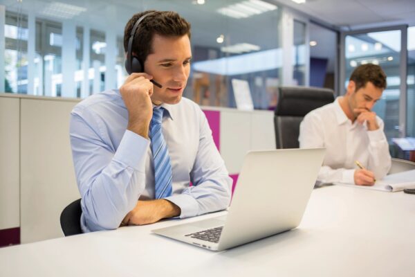 A person sitting in front of a laptop wearing a headset and talking