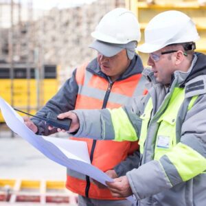 Two people wearing safety jackets and discussing over a doccument