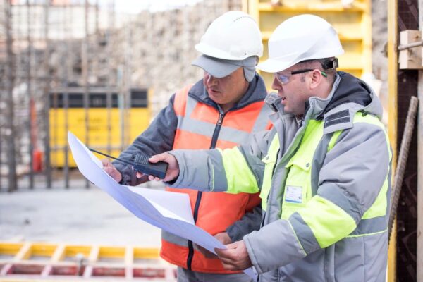 Two people wearing safety jackets and discussing over a doccument